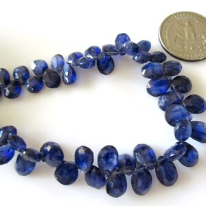 May include: A strand of dark blue gemstone beads, each bead is faceted and oval shaped. The beads are approximately the size of a US quarter.