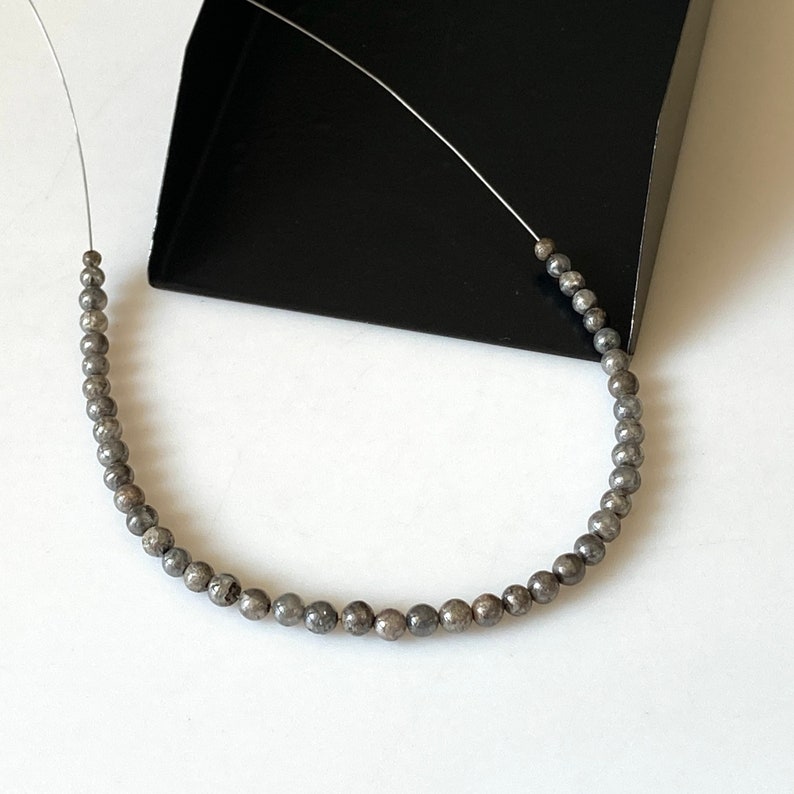 May include: A strand of silver-toned beads with a speckled finish, strung on a thin wire.