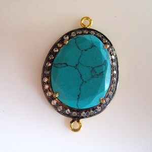 May include: A turquoise gemstone pendant with a silver and gold setting. The pendant is oval shaped and has a detailed design. It is surrounded by small clear stones.