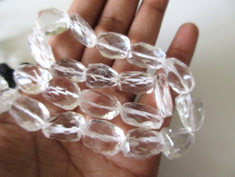 K&ouml;nnte beinhalten: Eine Str&auml;hne aus klaren Quarzkristallperlen, facettiert und oval geformt. Die Perlen sind auf einem durchsichtigen Faden aufgereiht und haben einen Durchmesser von etwa 10 mm.