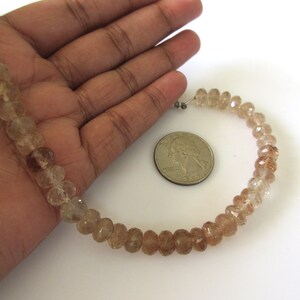 May include: A strand of light brown faceted gemstone beads, approximately 16 inches long, with a diameter of about 6mm. The beads are strung on a clear elastic cord and are displayed on a hand for size comparison.