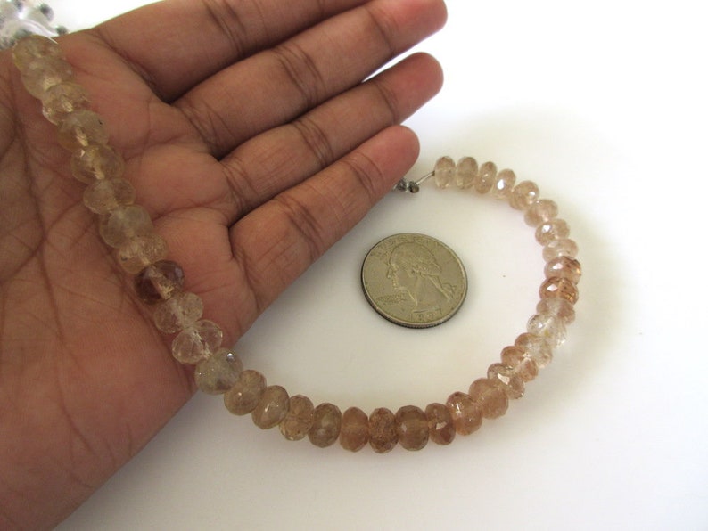 May include: A strand of light brown faceted gemstone beads, approximately 16 inches long, with a diameter of about 6mm. The beads are strung on a clear elastic cord and are displayed on a hand for size comparison.