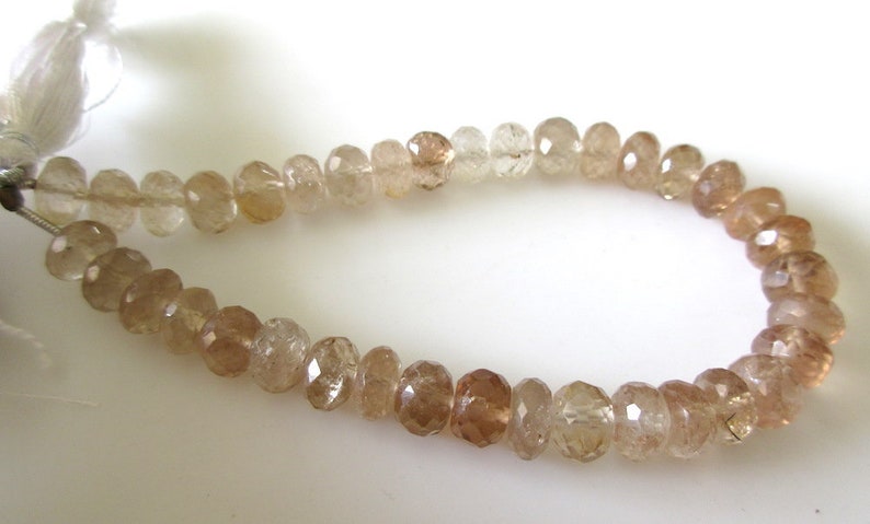 May include: A strand of faceted, translucent brown gemstone beads. The beads are strung on a white thread and are approximately 6mm in diameter.