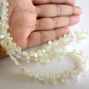 May include: A strand of white opal gemstone beads in a teardrop shape. The beads are strung on a clear thread and are arranged in a loose, flowing pattern.