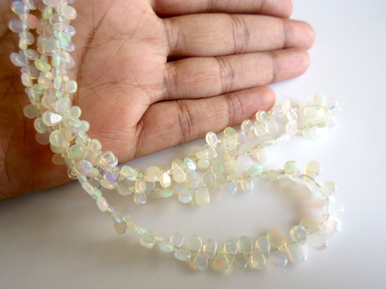 May include: A strand of white opal gemstone beads in a teardrop shape. The beads are strung on a clear thread and are arranged in a loose, flowing pattern.