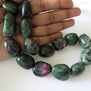 May include: A strand of polished, oval-shaped gemstones. The stones are a mix of deep green and dark red, with a smooth, glossy finish. The gemstones are strung together on a white cord, ready for jewelry making.