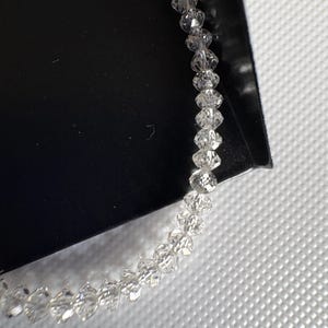 Puede incluir: Una delicada pulsera compuesta por numerosas cuentas claras y facetadas. Las cuentas est&aacute;n ensartadas, creando un accesorio brillante y elegante. La pulsera se muestra sobre un fondo blanco y negro.