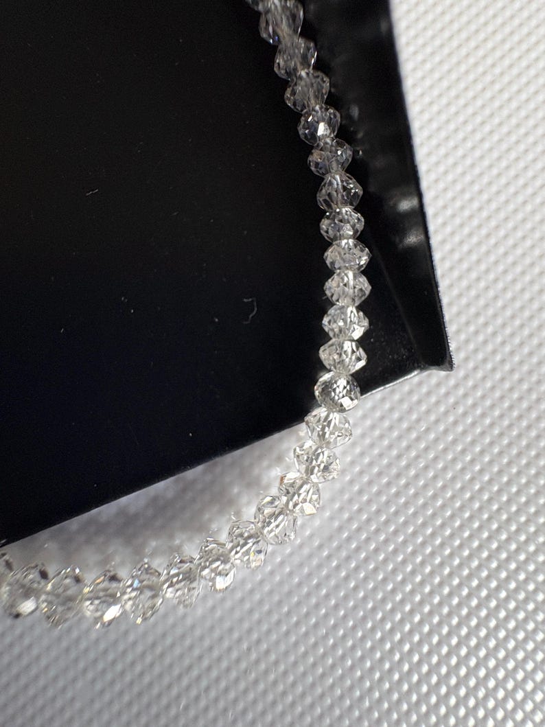 Puede incluir: Una delicada pulsera compuesta por numerosas cuentas claras y facetadas. Las cuentas est&aacute;n ensartadas, creando un accesorio brillante y elegante. La pulsera se muestra sobre un fondo blanco y negro.