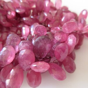 May include: A strand of pink faceted gemstone beads. The beads are oval shaped and have a smooth, polished finish.
