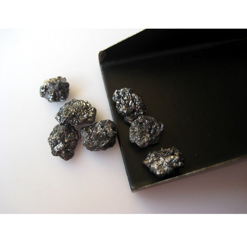 Puede incluir: Un grupo de diamantes negros, algunos en una sart&eacute;n de metal negro, otros esparcidos sobre una superficie blanca.