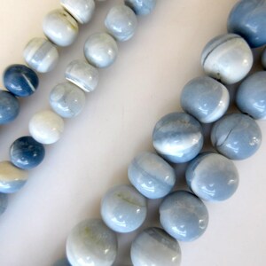 May include: A strand of blue and white opal beads. The beads are round and have a smooth, polished finish. The beads are strung on a clear thread.