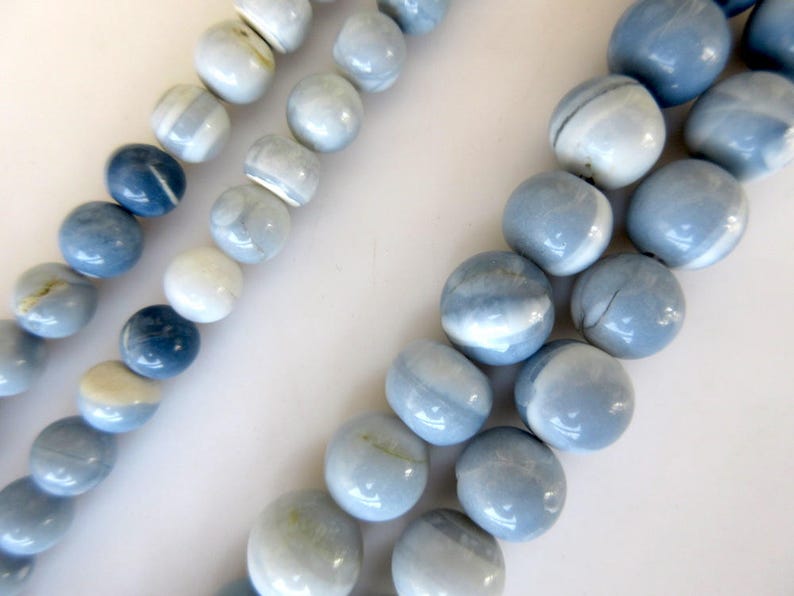 May include: A strand of blue and white opal beads. The beads are round and have a smooth, polished finish. The beads are strung on a clear thread.