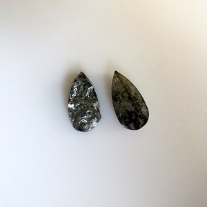 May include: Two teardrop-shaped black and silver stones with a rough, textured surface.
