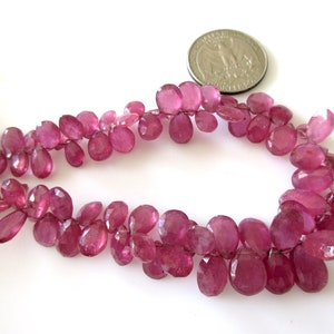 May include: A strand of pink gemstone beads, likely ruby, in a faceted oval shape. The beads are strung on a wire and are approximately 1/2 inch in length.