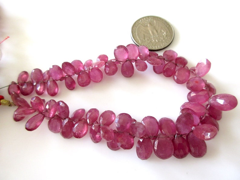 May include: A strand of pink gemstone beads, likely ruby, in a faceted oval shape. The beads are strung on a wire and are approximately 1/2 inch in length.
