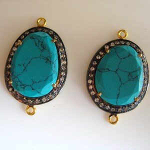 May include: Two turquoise gemstone pendants with gold settings and a border of small clear stones. The pendants have a loop at the top for attaching to a chain or cord.