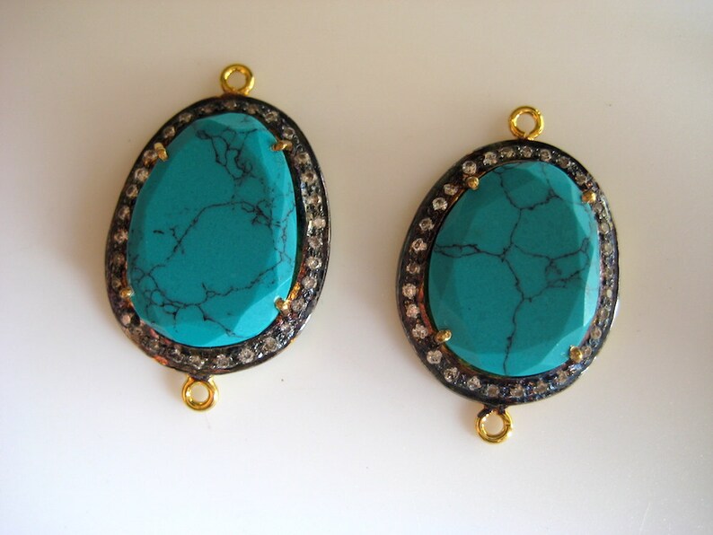 May include: Two turquoise gemstone pendants with gold settings and a border of small clear stones. The pendants have a loop at the top for attaching to a chain or cord.