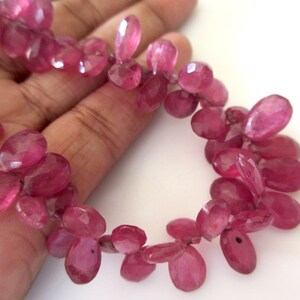 May include: A strand of pink gemstone beads, each bead is oval shaped and faceted. The beads are strung on a clear thread.