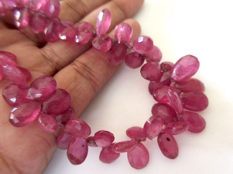 May include: A strand of pink gemstone beads, each bead is oval shaped and faceted. The beads are strung on a clear thread.