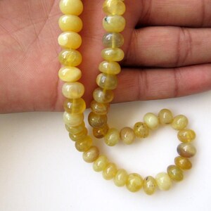 May include: A strand of yellow opal beads, strung on a cord, with a round shape. The beads are arranged in a circular pattern, with a few beads hanging loose.