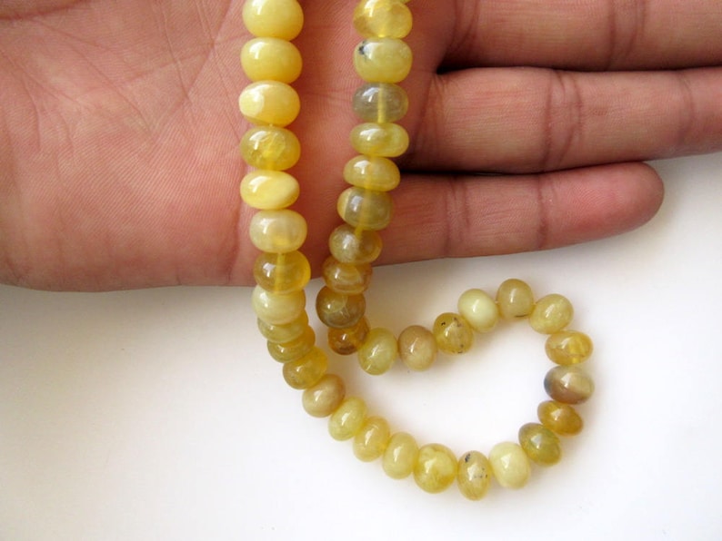 May include: A strand of yellow opal beads, strung on a cord, with a round shape. The beads are arranged in a circular pattern, with a few beads hanging loose.