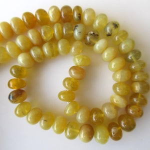 May include: A strand of yellow opal beads, some with black inclusions, strung on a white background.