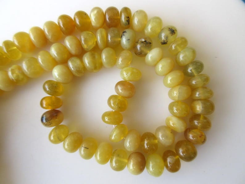 May include: A strand of yellow opal beads, some with black inclusions, strung on a white background.