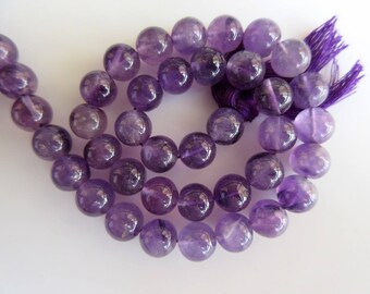 May include: A strand of purple amethyst beads, each bead is round and smooth. The beads are strung on a cord with a purple tassel at the end.