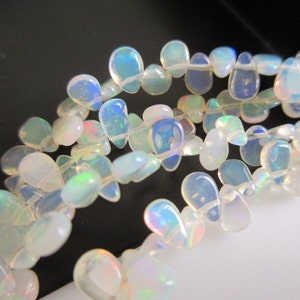 May include: A strand of iridescent white opal teardrop beads. The beads are strung on a clear thread and are arranged in a loose, flowing pattern.