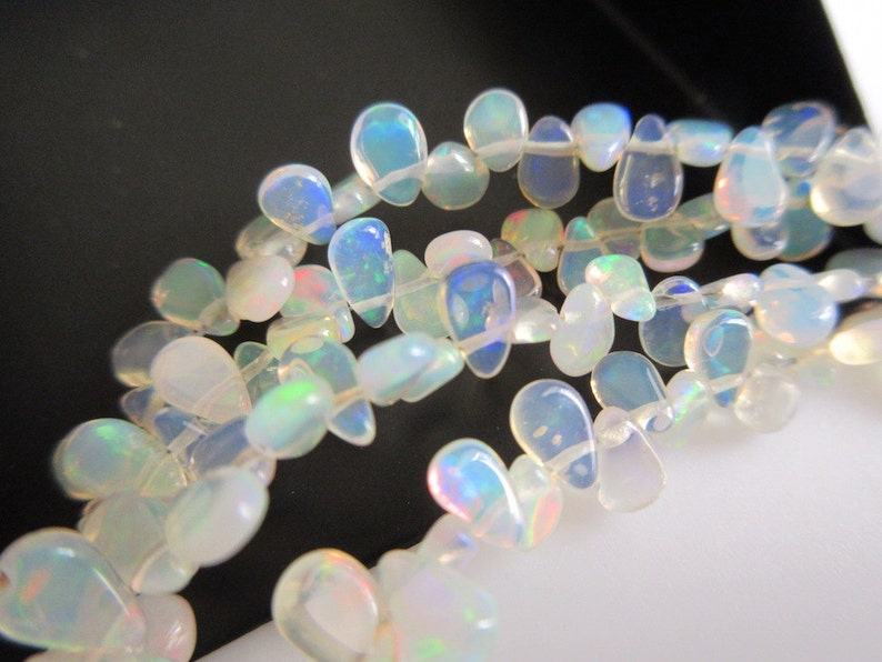 May include: A strand of iridescent white opal teardrop beads. The beads are strung on a clear thread and are arranged in a loose, flowing pattern.