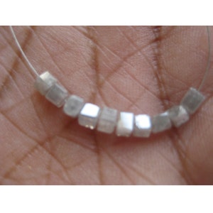 May include: A strand of white, square-shaped beads made from natural rough diamonds. The beads are strung on a thin wire.