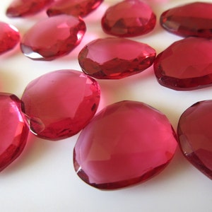 May include: A group of 12 faceted, clear, pink glass stones. The stones are oval shaped and have a smooth, polished finish.