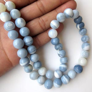 May include: A strand of blue and white opal beads, with a light blue and white color gradient. The beads are round and smooth, and they are strung on a white thread.