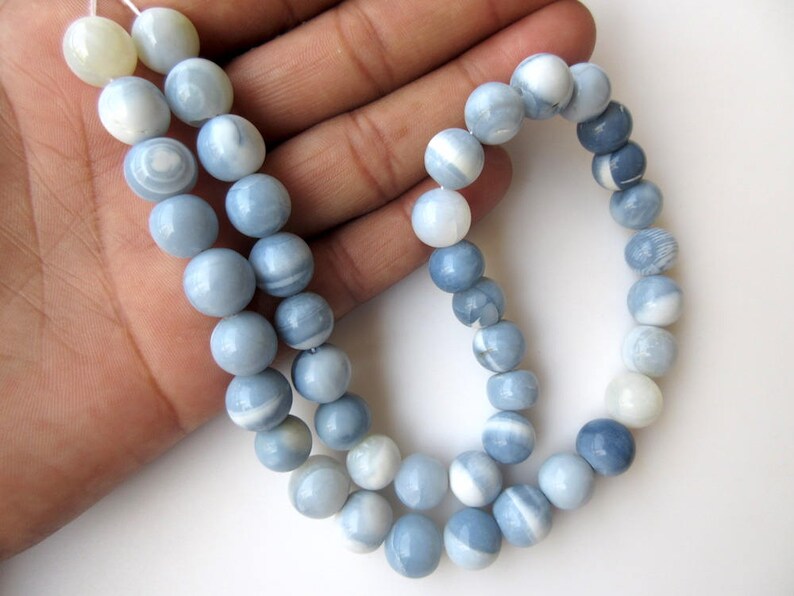 May include: A strand of blue and white opal beads, with a light blue and white color gradient. The beads are round and smooth, and they are strung on a white thread.