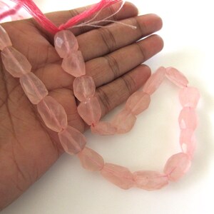 May include: A strand of pink rose quartz beads, faceted and polished, with a slightly irregular shape. The beads are strung on a thin, pink thread.
