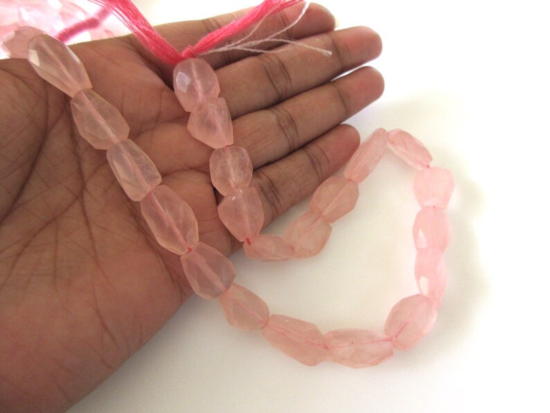 May include: A strand of pink rose quartz beads, faceted and polished, with a slightly irregular shape. The beads are strung on a thin, pink thread.