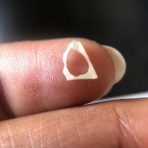 May include: A small, white, translucent, triangular-shaped piece of glass with a hole in the center.