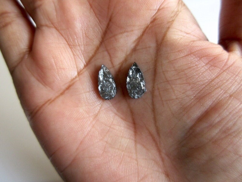 May include: Two small, pear-shaped, black diamonds on a hand.