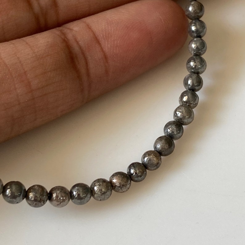 May include: A strand of small, round, dark gray beads. The beads have a speckled, textured surface.