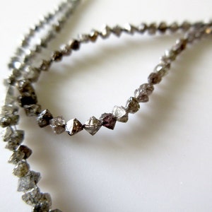 May include: A strand of grey and black diamond beads. The beads are faceted and have a rough, natural look.