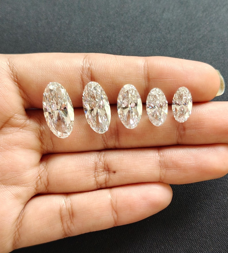 May include: Five clear, colorless, oval-cut gemstones arranged in a row by size from largest to smallest. Each stone features a faceted surface that reflects light, creating a brilliant, sparkling appearance with sharp, defined edges.