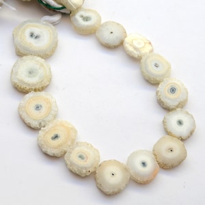 May include: A strand of white crystal beads with a circular, layered design. The beads have a translucent, milky white color with a slight shimmer.