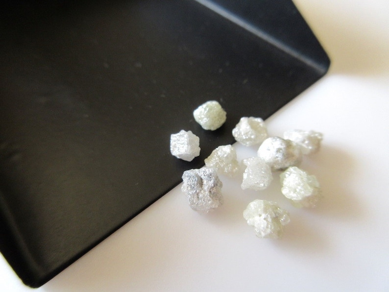 Puede incluir: Primer plano de un peque&ntilde;o mont&oacute;n de diamantes en bruto blancos sobre una superficie blanca. Los diamantes son de diversas formas y tama&ntilde;os.