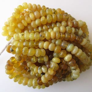 May include: A strand of yellow opal beads, each bead is round and smooth. The beads are piled together in a heap.