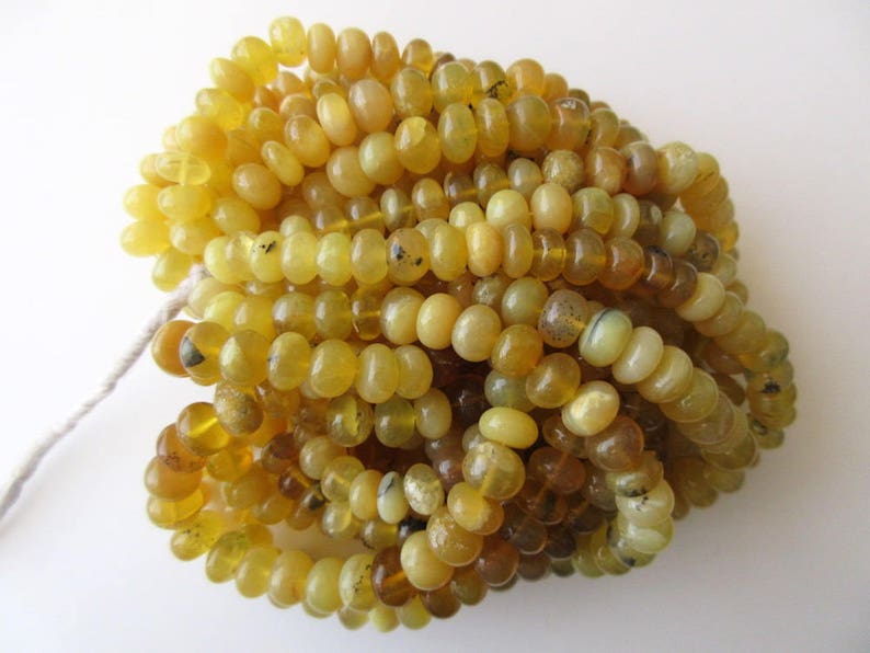 May include: A strand of yellow opal beads, each bead is round and smooth. The beads are piled together in a heap.