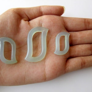 May include: Three jade-coloured, open-shaped pendants in varying sizes. The pendants have a smooth, translucent appearance and are arranged on a light-toned background. The shapes are reminiscent of stylized leaves or teardrops, suitable for jewellery making.