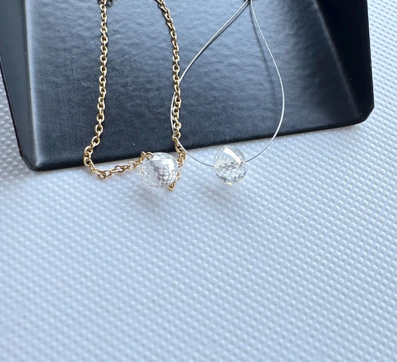 K&ouml;nnte beinhalten: Zwei Halsketten mit klaren, facettierten, runden Perlen. Eine Halskette besteht aus einer goldfarbenen Metallkette, w&auml;hrend die andere auf einer d&uuml;nnen, transparenten Monofilamentschnur aufgezogen ist. Beide Ketten haben eine einzelne Perle.
