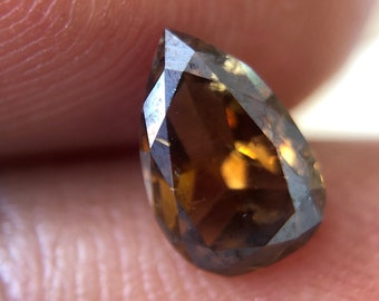 May include: A pear-shaped brown diamond with a faceted cut. The diamond has a warm, golden hue.