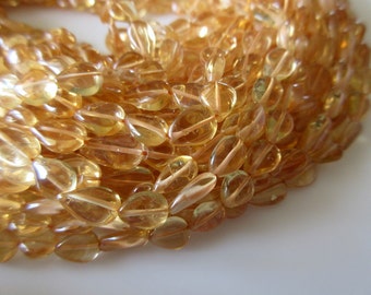 Könnte beinhalten: Eine Strähne aus durchscheinenden, goldgelben Edelsteinperlen in Tropfenform. Die Perlen sind auf einem dünnen, durchsichtigen Faden aufgefädelt.