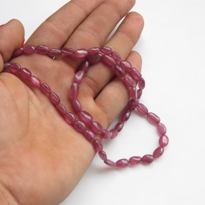 Op de afbeelding: Een streng roze ovale edelsteen kralen. De kralen zijn geregen op een doorzichtige draad en zijn ongeveer 6 mm groot.